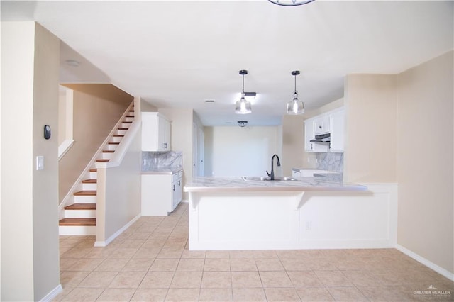 kitchen with decorative light fixtures, white cabinetry, sink, backsplash, and kitchen peninsula