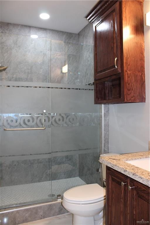 bathroom featuring vanity, toilet, tile walls, and a shower with shower door