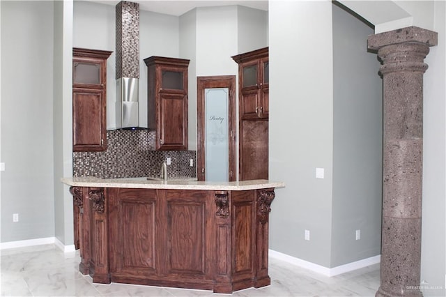 kitchen featuring backsplash, ventilation hood, a kitchen breakfast bar, kitchen peninsula, and decorative columns