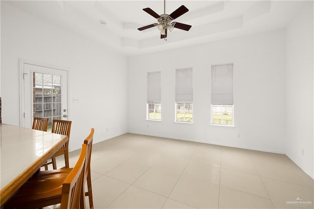 unfurnished dining area with ceiling fan, a tray ceiling, and light tile patterned floors