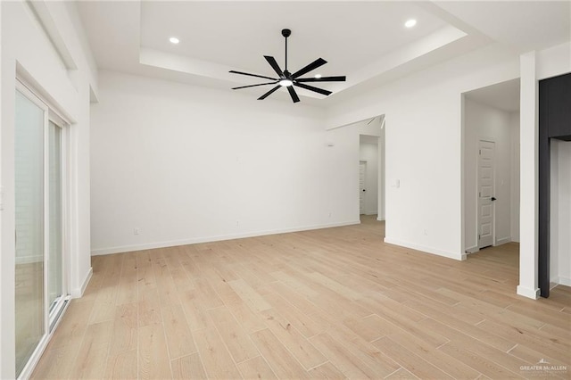 interior space with ceiling fan, a tray ceiling, and light wood-type flooring