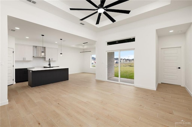 living room featuring ceiling fan, sink, a raised ceiling, and light hardwood / wood-style floors