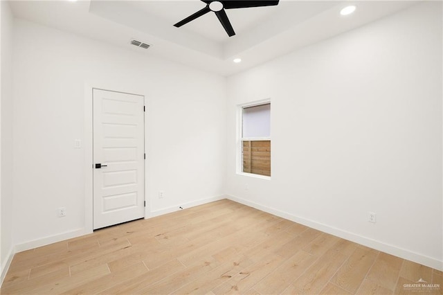 empty room featuring a tray ceiling, light hardwood / wood-style floors, and ceiling fan