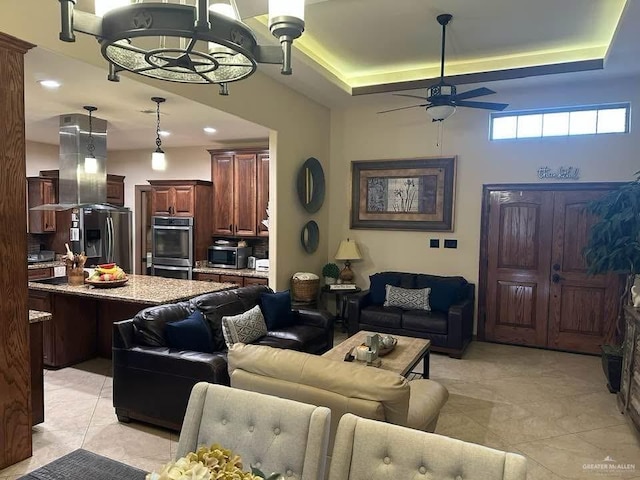 living room with a tray ceiling, light tile patterned flooring, and ceiling fan with notable chandelier