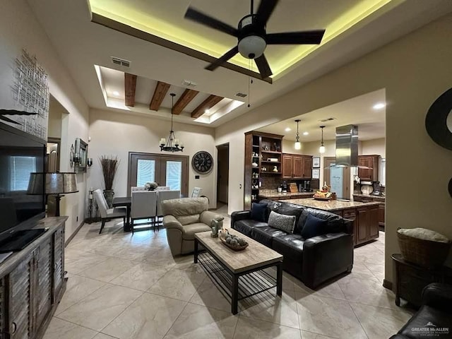 living room with beamed ceiling, ceiling fan with notable chandelier, and a tray ceiling