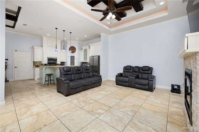 living area featuring a ceiling fan, crown molding, recessed lighting, a stone fireplace, and a tray ceiling