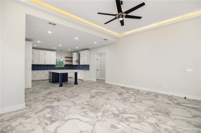 kitchen with a center island, wall chimney range hood, decorative backsplash, white cabinetry, and a breakfast bar area