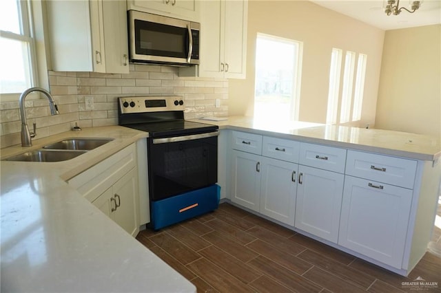 kitchen featuring wood finish floors, stainless steel appliances, light countertops, a sink, and a peninsula