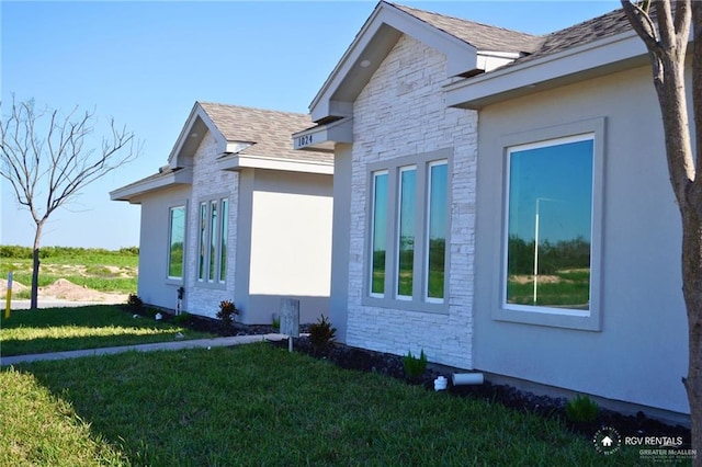 view of property exterior with a yard, a shingled roof, stone siding, and stucco siding