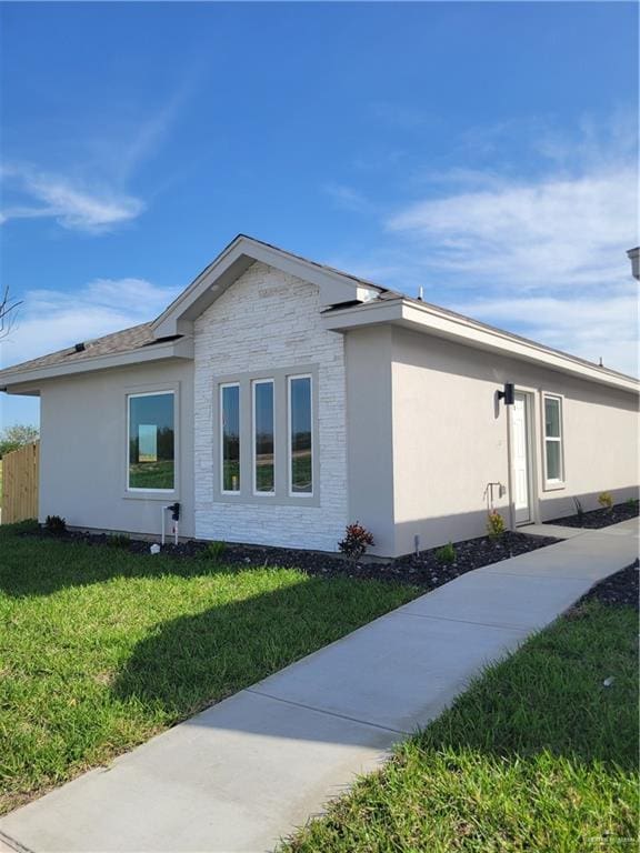 view of property exterior featuring a yard, stone siding, fence, and stucco siding