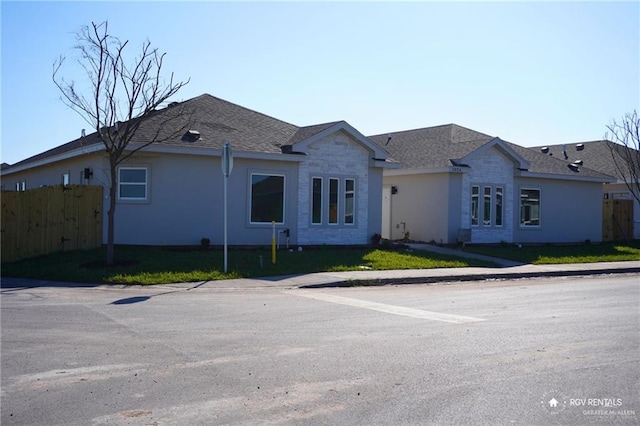 ranch-style home with a front lawn, roof with shingles, and fence