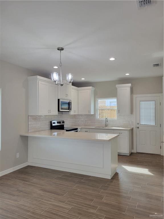 kitchen with stainless steel appliances, dark wood-type flooring, a peninsula, a sink, and light countertops