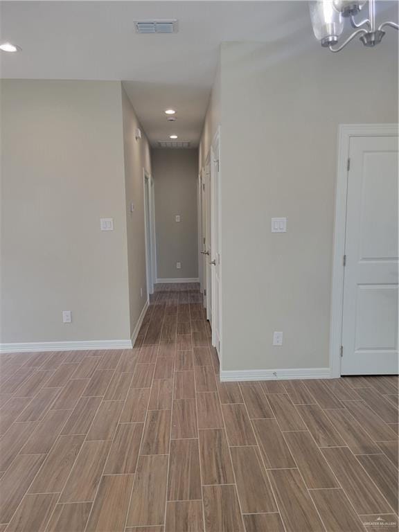 unfurnished room with a chandelier, wood tiled floor, visible vents, and baseboards