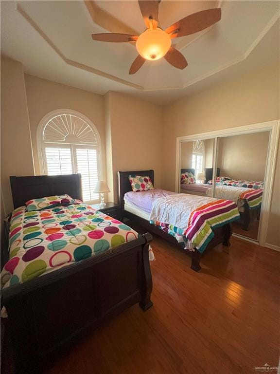 bedroom with wood-type flooring, a raised ceiling, and ceiling fan