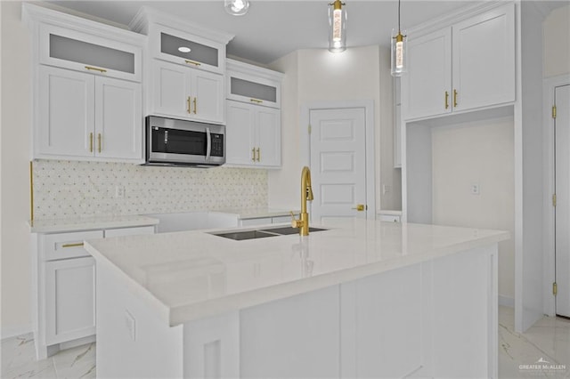 kitchen with marble finish floor, a center island with sink, a sink, stainless steel microwave, and backsplash