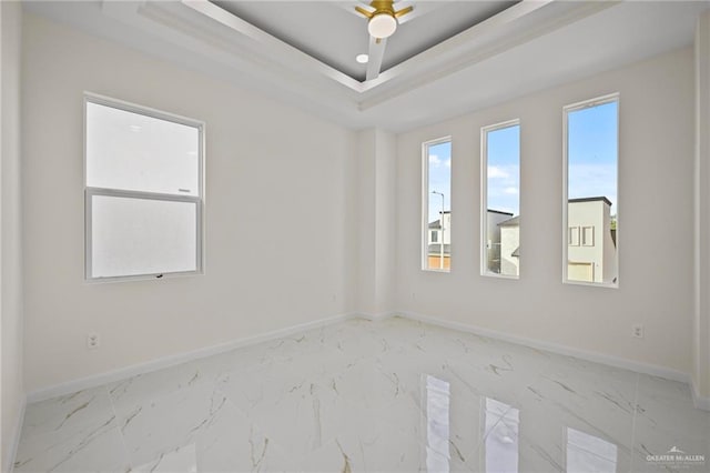 unfurnished room with a tray ceiling, baseboards, and marble finish floor