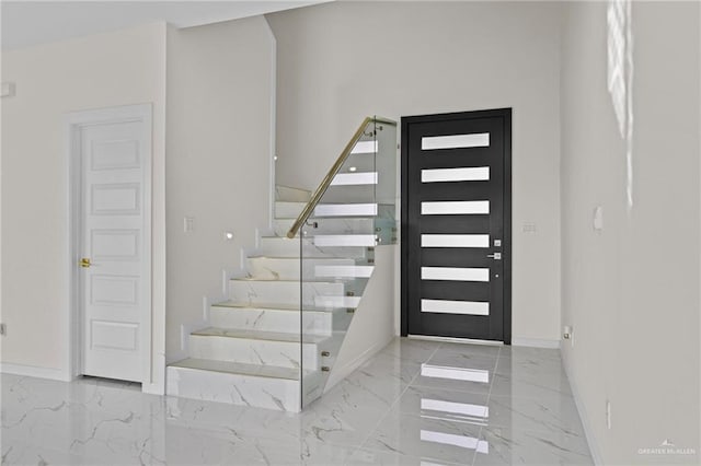 entryway with marble finish floor, stairs, and baseboards