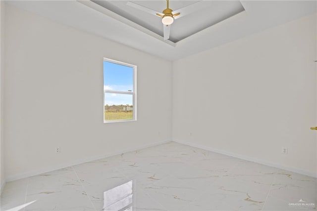 unfurnished room with a raised ceiling, baseboards, and marble finish floor