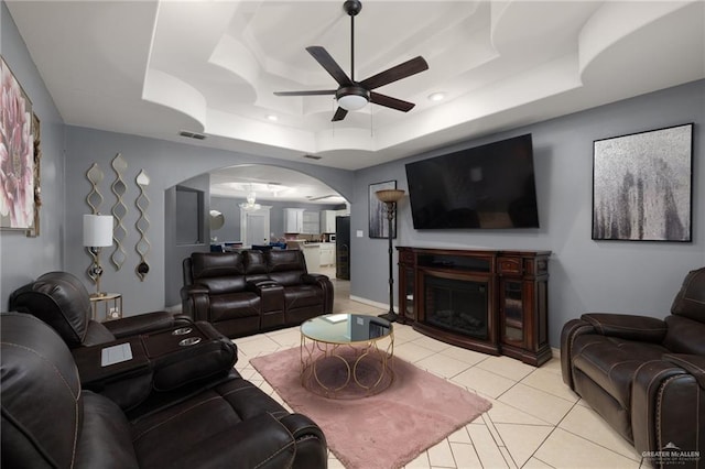 living area featuring light tile patterned floors, a tray ceiling, arched walkways, and a glass covered fireplace