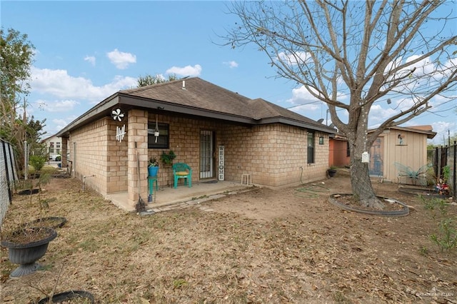 back of property featuring an outbuilding, a storage shed, fence, roof with shingles, and a patio area