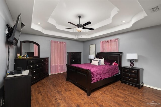 bedroom with dark wood-style floors, a tray ceiling, and visible vents