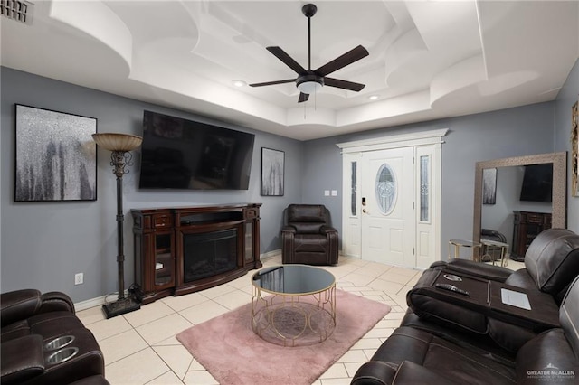 living room with light tile patterned flooring, visible vents, a ceiling fan, a raised ceiling, and a glass covered fireplace