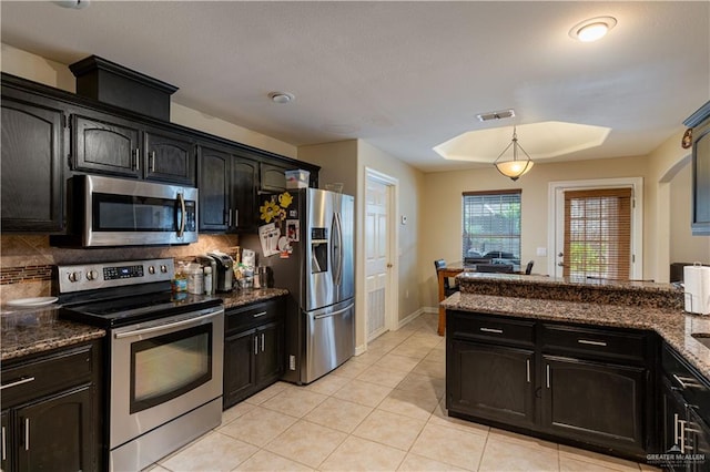 kitchen featuring decorative backsplash, appliances with stainless steel finishes, hanging light fixtures, and dark stone counters