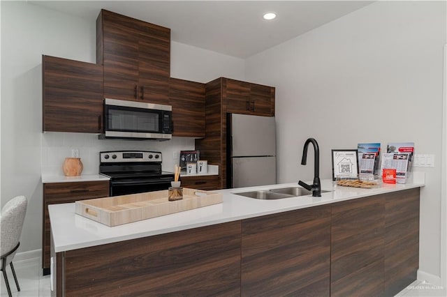 kitchen with kitchen peninsula, appliances with stainless steel finishes, tasteful backsplash, dark brown cabinetry, and sink