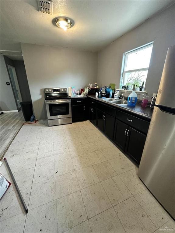 kitchen with visible vents, light floors, dark cabinetry, stainless steel appliances, and a sink