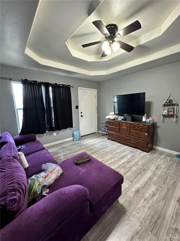 living room with a ceiling fan, a tray ceiling, wood finished floors, and baseboards