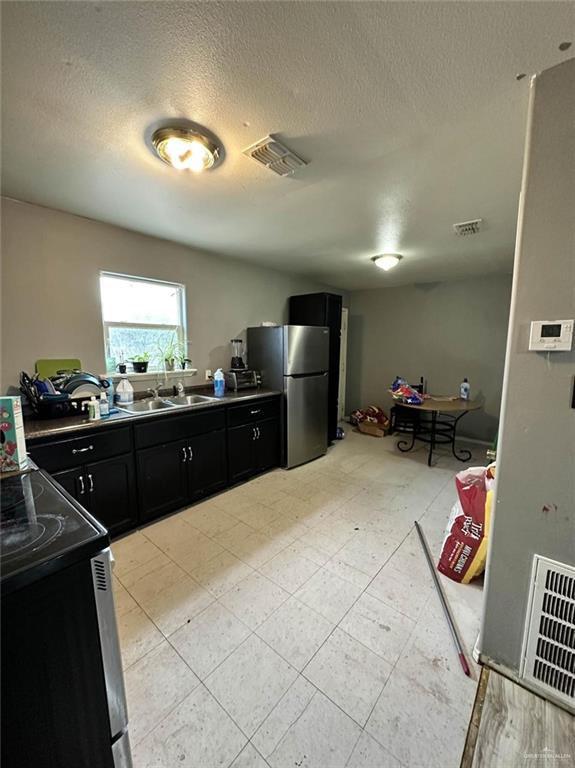 kitchen featuring dark cabinetry, visible vents, freestanding refrigerator, a sink, and range with electric stovetop