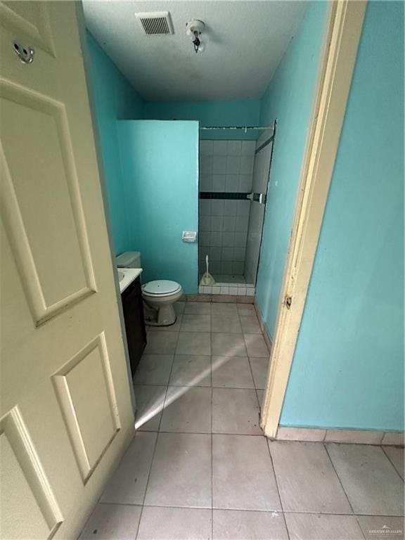 bathroom with vanity, tile patterned flooring, tiled shower, and toilet