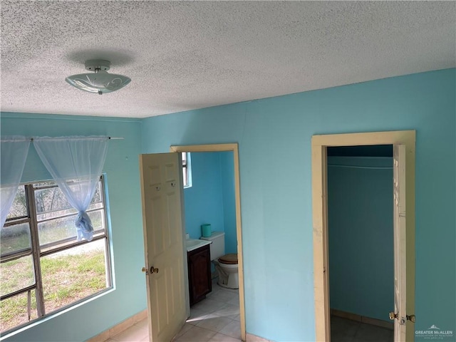 bedroom with ensuite bathroom, light tile patterned floors, and a textured ceiling