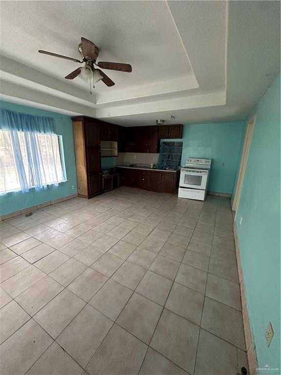 kitchen with dark brown cabinetry, ceiling fan, electric range, a tray ceiling, and light tile patterned floors