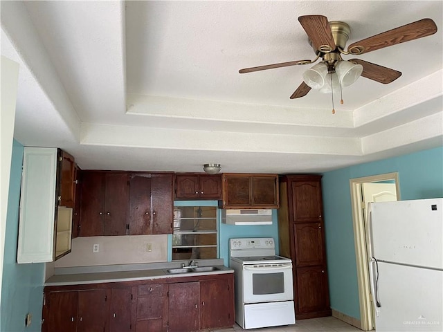 kitchen featuring white appliances, dark brown cabinetry, ceiling fan, a tray ceiling, and sink