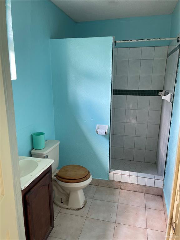 bathroom featuring tile patterned floors, toilet, vanity, and a tile shower