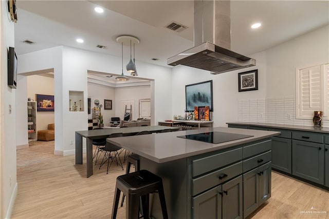 kitchen featuring pendant lighting, a kitchen island, black electric stovetop, island range hood, and light wood-type flooring