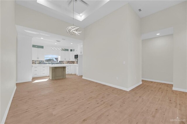 323 Santa Isabel, Rio Grande City, TX 78582 - unfurnished living room featuring light wood finished floors, a chandelier, baseboards, a towering ceiling, and a sink