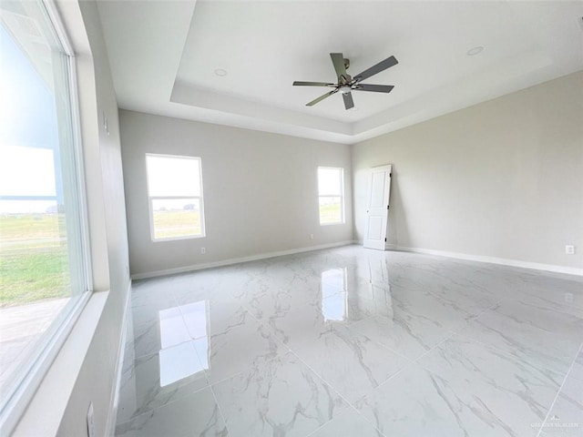 empty room featuring a tray ceiling, ceiling fan, and a healthy amount of sunlight