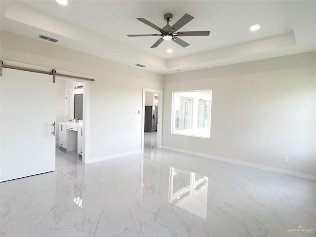 unfurnished room featuring ceiling fan, a barn door, and a tray ceiling