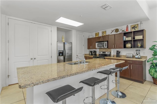 kitchen with sink, a kitchen bar, stainless steel appliances, and an island with sink