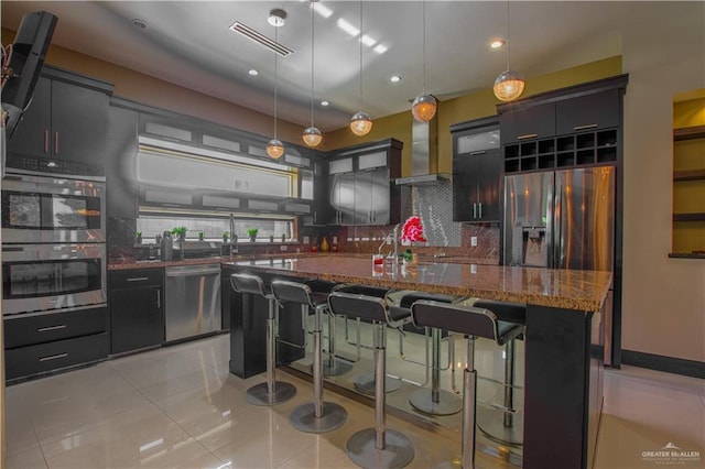 309 N Mockingbird Ave, Mission, TX 78572 - kitchen with stainless steel appliances, tasteful backsplash, wall chimney exhaust hood, a breakfast bar area, and dark stone counters
