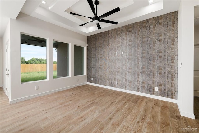 unfurnished room featuring ceiling fan, a raised ceiling, and light wood-type flooring