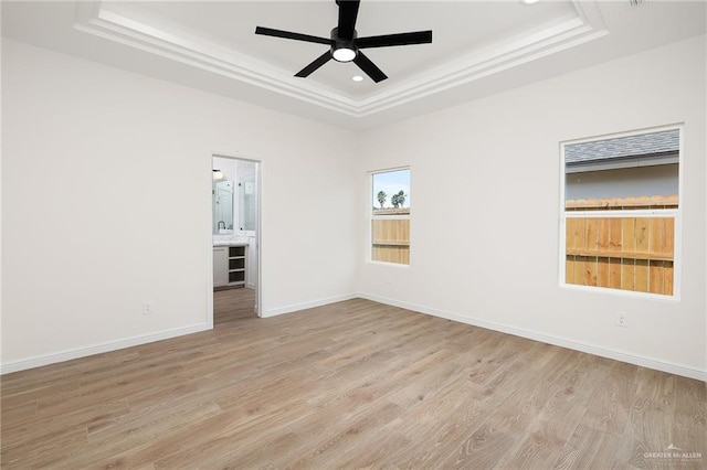 spare room with light wood-type flooring, a raised ceiling, and ceiling fan