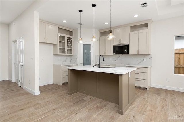 kitchen with decorative light fixtures, light hardwood / wood-style flooring, a kitchen island with sink, and sink