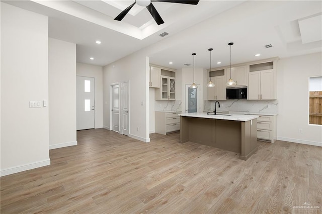 kitchen featuring decorative light fixtures, light hardwood / wood-style floors, and an island with sink