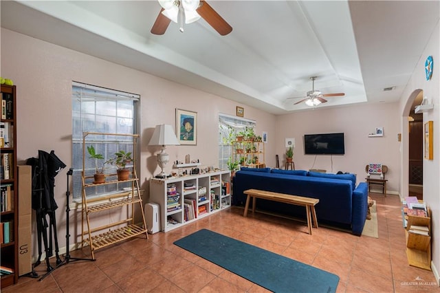 living area with a tray ceiling, arched walkways, visible vents, ceiling fan, and tile patterned floors