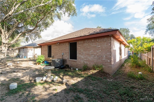 back of house featuring central AC unit, fence, and brick siding