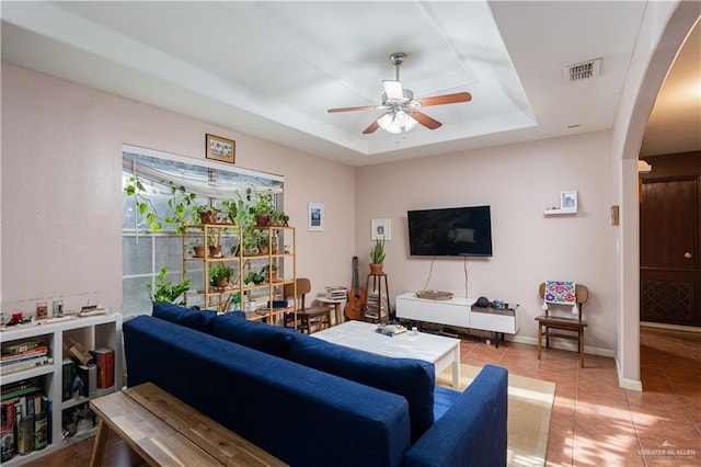 living area featuring visible vents, arched walkways, ceiling fan, a tray ceiling, and light tile patterned flooring