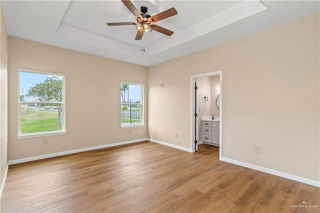 unfurnished bedroom featuring a tray ceiling, ensuite bath, ceiling fan, and light hardwood / wood-style flooring